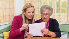 Mladá žena pomáhá seniorce s dokumentem, společné vyřizování papírů u stolu