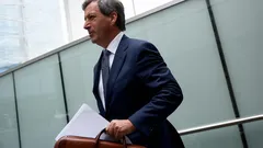Obchodník v obleku s aktovkou a dokumenty jde moderní kancelářskou budovou.