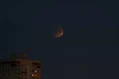Měsíční zatmění na noční obloze nad městskou budovou, tmavá atmosféra v Praze